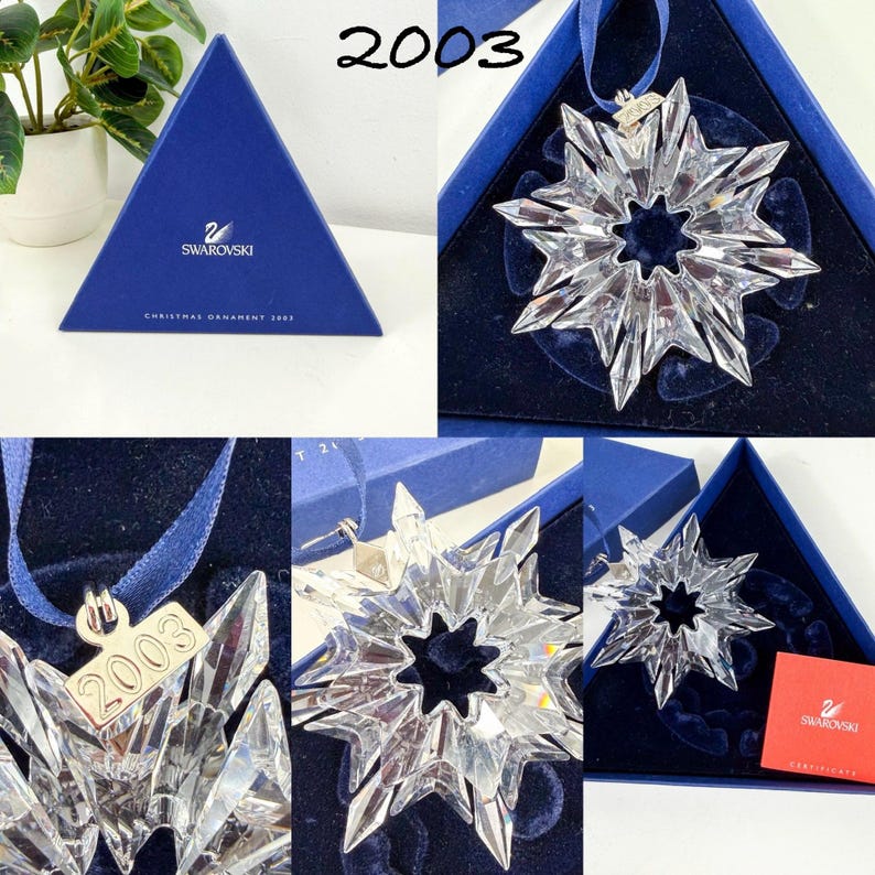 May include: A clear crystal snowflake ornament with a blue ribbon and a metal tag engraved with the year 2003. The ornament is presented in a triangular blue box with the Swarovski logo and includes a red certificate of authenticity card.