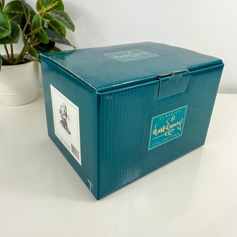 Op de afbeelding: Een turquoise doos met de woorden "Classics" en "Walt Disney Collection" in gouden letters. De doos heeft een wit etiket met een zwart-wit afbeelding en een barcode. Een kleine plant in een pot staat op de achtergrond.