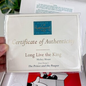 Op de afbeelding: Een certificaat van echtheid van de Disney Classics Collection. Het cr&egrave;mekleurige certificaat heeft gouden letters met de tekst "Certificate of Authenticity" en "Long Live the King". Het vermeldt Mickey Mouse uit Disney's "The Prince and the Pauper".