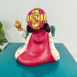 Op de afbeelding: Een keramieken beeldje van een personage met een gouden kroon en een gouden scepter. Het beeldje is gekleed in een rode en witte cape met zwarte accenten. Het personage heeft zwarte oren en een groene outfit.