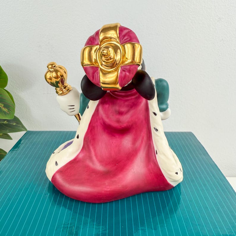 Op de afbeelding: Een keramieken beeldje van een personage met een gouden kroon en een gouden scepter. Het beeldje is gekleed in een rode en witte cape met zwarte accenten. Het personage heeft zwarte oren en een groene outfit.
