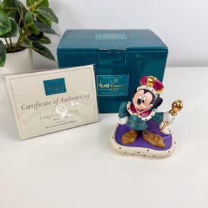 Op de afbeelding: Een Mickey Mouse-beeldje uit de Walt Disney Classics Collection, gekleed als koning. Het beeldje draagt een kroon en houdt een scepter vast. De doos en het certificaat van echtheid zijn ook zichtbaar.