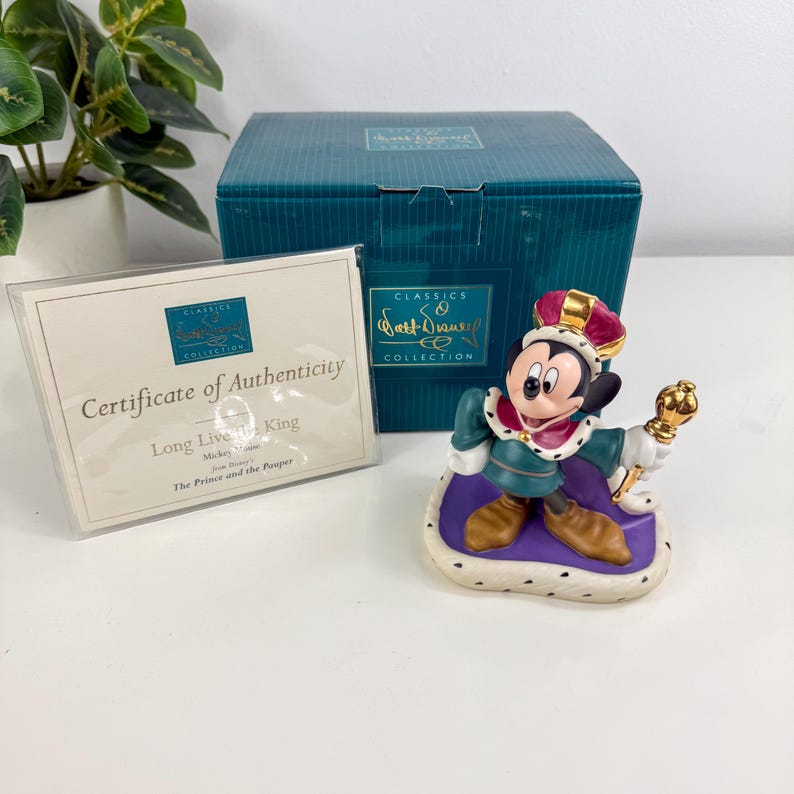 Op de afbeelding: Een Mickey Mouse-beeldje uit de Walt Disney Classics Collection, gekleed als koning. Het beeldje draagt een kroon en houdt een scepter vast. De doos en het certificaat van echtheid zijn ook zichtbaar.