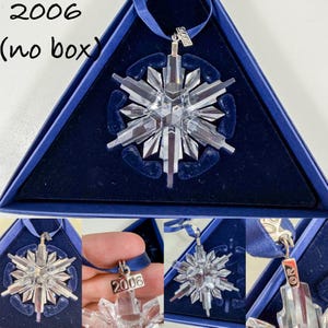 May include: A clear crystal snowflake ornament with a blue ribbon hanger. A silver-toned metal tag attached to the ribbon is engraved with the year 2006. The ornament is displayed within a dark blue triangular case with a velvet-like interior.