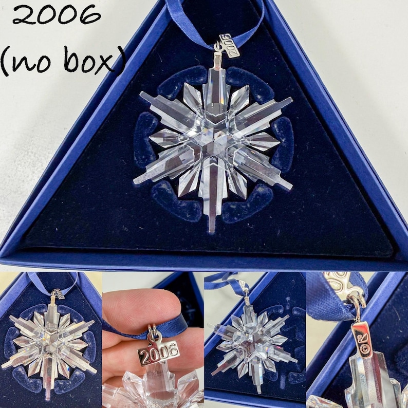 May include: A clear crystal snowflake ornament with a blue ribbon hanger. A silver-toned metal tag attached to the ribbon is engraved with the year 2006. The ornament is displayed within a dark blue triangular case with a velvet-like interior.