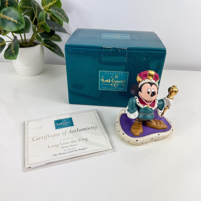 Op de afbeelding: Een Mickey Mouse-beeldje uit de Walt Disney Classics Collection, gekleed als koning. Het beeldje staat op een paarse en witte basis, draagt een groene en rode outfit en een gouden kroon. De doos en het certificaat zijn ook zichtbaar.