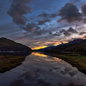 May include: A scenic view of a lake with mountains in the background. The sky is a mix of blue, pink, and orange, with clouds reflecting in the water.
