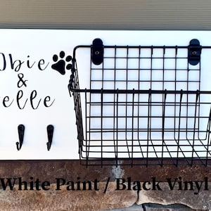 May include: White wooden sign with black paw prints and the text "Obie & Belle" with three black hooks and a black wire basket attached.