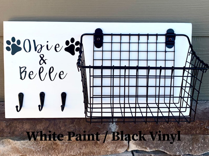 May include: White wooden sign with black paw prints and the text "Obie & Belle" with three black hooks and a black wire basket attached.