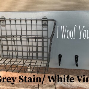 May include: Grey wooden dog leash holder with a wire basket, three hooks, and white vinyl lettering that says "I Woof You" with paw prints.