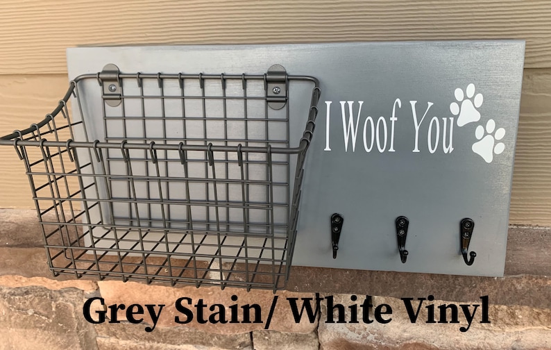 May include: Grey wooden dog leash holder with a wire basket, three hooks, and white vinyl lettering that says "I Woof You" with paw prints.