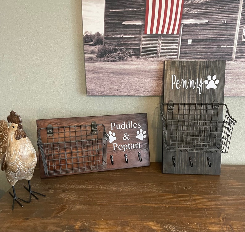 May include: Two wooden key hooks with wire baskets and paw print designs. The top hook says "Penny" and the bottom hook says "Puddles & Poptart".