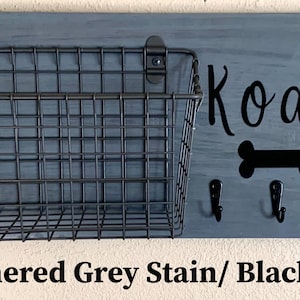 May include: A weathered grey wooden dog leash holder with a black wire basket, three hooks, and black vinyl lettering that says "Koda" with a paw print and bone design.