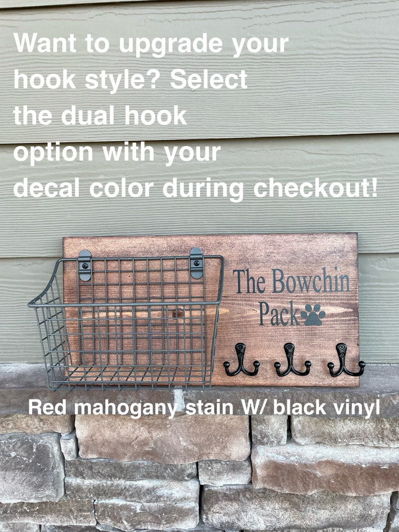 May include: A wooden sign with the text "The Bowchin Pack" and a paw print. The sign has three black hooks and a wire basket underneath. The sign is stained red mahogany with black vinyl lettering.