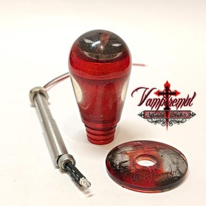 May include: A red and black glitter resin arcade stick ball top with a metallic base, a silver metal shaft with an attached LED wire, and a matching circular resin dust washer featuring a cross symbol and the text Vampiremil Arcade Sticks.