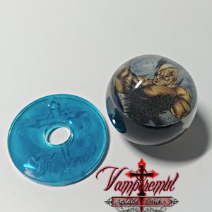 Peut inclure: Une rondelle translucide bleue et un pommeau de joystick rond et transparent avec un graphisme de personnage. Le pommeau de la boule représente une figure musclée dans une posture de combat. Le logo "Vampremtul Arcade Sticks" est visible.