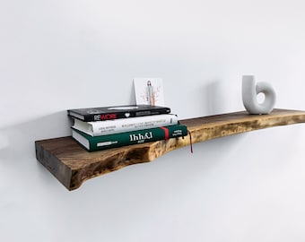 Puede incluir: Una estantería de madera con un borde vivo, que presenta una pila de libros y un jarrón de cerámica blanco. Los libros incluyen títulos como "Rework" e "Ihh&I".