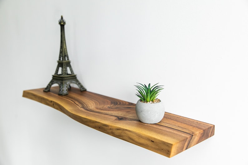 Pode incluir: Uma prateleira de madeira com uma planta suculenta viva em um vaso cinza e uma pequena figura da Torre Eiffel. A prateleira &eacute; feita de madeira natural com uma borda viva e uma cor marrom escura.