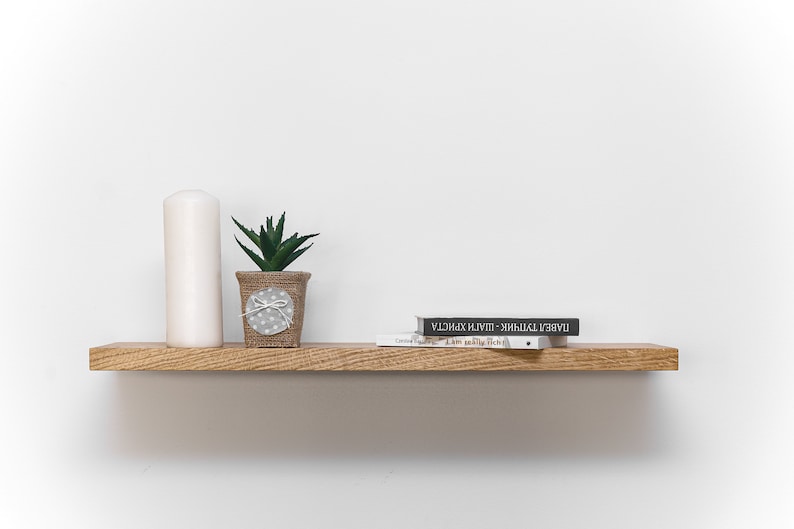 May include: A wooden shelf with a white candle, a small potted succulent plant, and two books. The top book is black with white text that reads "LABELS - ЖИВЫЙ - PLAIN - ХАРАКТЕР". The bottom book is white with black text that reads "I Am Really Rich".