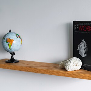 Pode incluir: Uma prateleira de madeira com um globo terrestre, um livro intitulado "Rework" e um peda&ccedil;o de coral no topo.