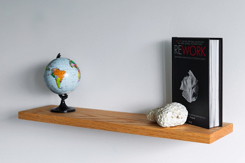 Pode incluir: Uma prateleira de madeira com um globo terrestre, um livro intitulado "Rework" e um peda&ccedil;o de coral no topo.