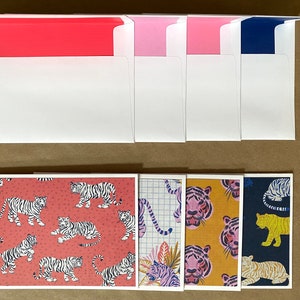 May include: Set of six blank greeting cards with envelopes. The cards feature a variety of colorful tiger designs. The envelopes are white with colored liners in pink, red, and blue.