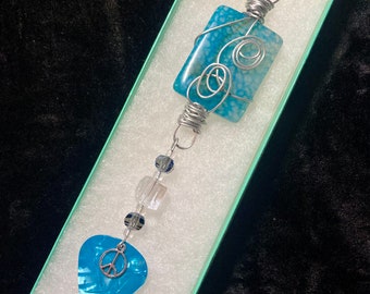 Adorno/atrapasol envuelto en alambre de medios mixtos con púa de guitarra azul nacarado, signo de la paz y caja de regalo.