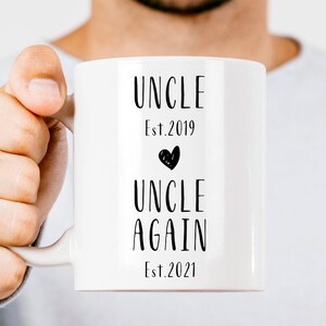 May include: White ceramic mug with black text that reads "Uncle Est. 2019" with a black heart symbol and "Uncle Again Est. 2021"