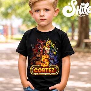 May include: A black short-sleeved t-shirt featuring a graphic print of four animated characters, a large number 5 with a pizza-slice pattern, and a glowing neon-style sign with the name CORTEZ printed in bold yellow capital letters.