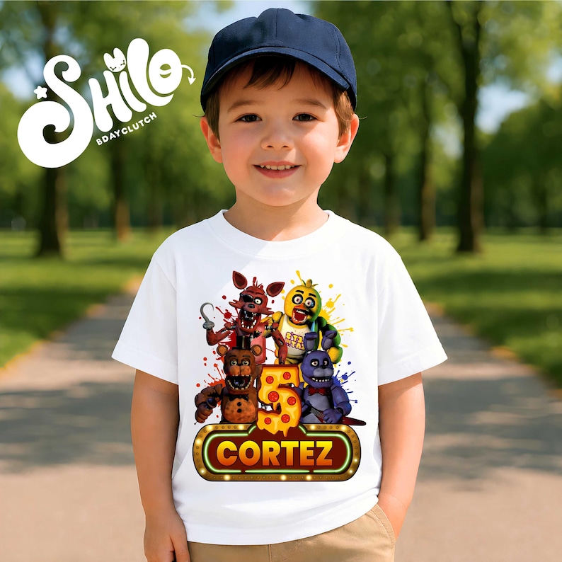 May include: A white short-sleeved t-shirt featuring a colorful graphic of four animatronic characters, a large yellow number five with pepperoni pizza patterns, and a glowing marquee sign displaying the name CORTEZ in bold orange letters.