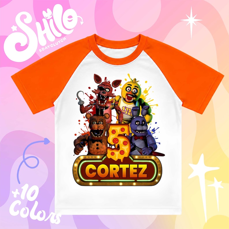 May include: A white t-shirt with orange raglan sleeves featuring a graphic of four animatronic characters, a large number five shaped like pizza, and a glowing sign with the name CORTEZ printed in bold yellow letters against a dark background.