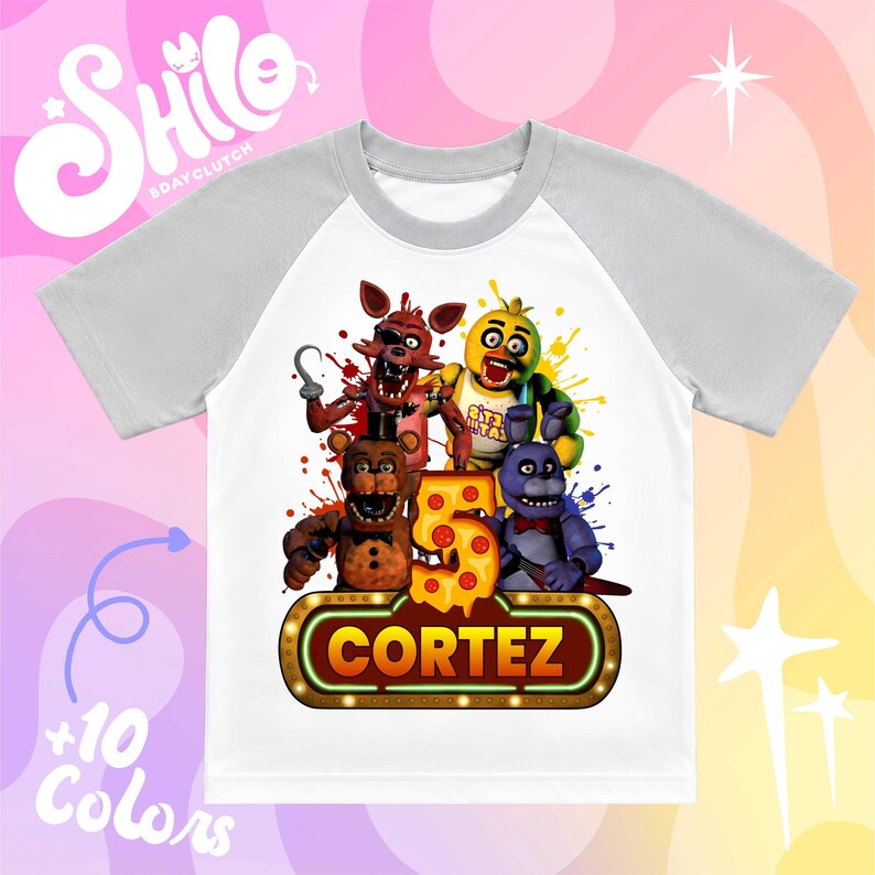 May include: A white t-shirt with gray raglan sleeves featuring a graphic of four animatronic characters, a large number five shaped like a pizza slice, and a glowing sign at the bottom with the name CORTEZ printed in bold yellow capital letters.