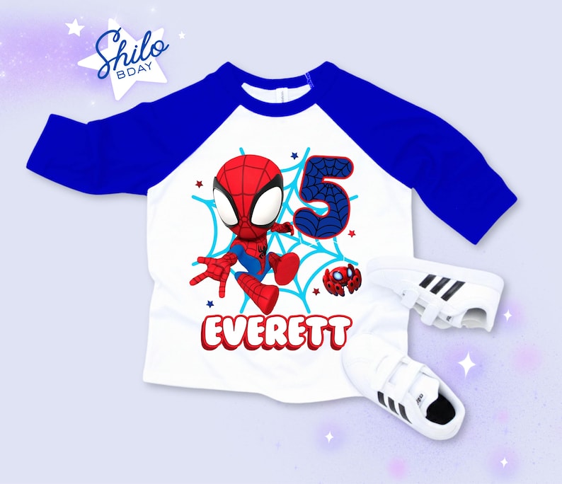 Pode incluir: Uma camisa branca e azul estilo raglan com um gr&aacute;fico do Homem-Aranha, o n&uacute;mero 5 e o nome "Everett" em vermelho. T&ecirc;nis brancos com listras pretas tamb&eacute;m est&atilde;o na imagem. A camisa &eacute; projetada para um anivers&aacute;rio.