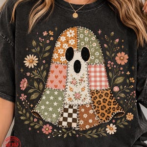 May include: A charcoal gray t-shirt featuring a central graphic of a ghost composed of various patchwork patterns including daisies, red hearts, pink gingham, leopard print, and black and white checkers, surrounded by floral illustrations.