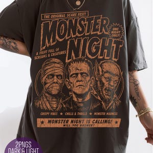 May include: A charcoal gray t-shirt featuring an orange graphic print with the text "MONSTER NIGHT," "THE ORIGINAL SCARE FEST!," "ONE NIGHT ONLY!," "A NIGHT FULL OF SCREAMS & CREATURES," "CREEPY VIBES," "CHILLS & THRILLS," "MONSTER MADNESS," and "MONSTER NIGHT IS CALLING! WILL YOU ANSWER?" depicting a mummy, Frankenstein's monster, and a werewolf.