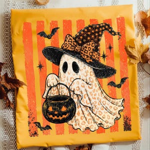 May include: A yellow fabric square featuring a central graphic of a ghost wearing a black witch hat with a leopard print bow and star pattern. The ghost has a leopard print body and holds a black jack-o'-lantern bucket, surrounded by bats.
