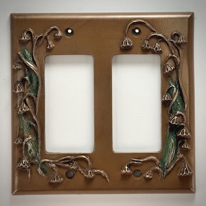May include: A double light switch cover plate with a decorative design of stylized lily of the valley flowers in shades of green and gold.