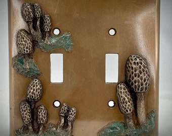 Peut inclure: Plaque de prise double de couleur bronze avec un relief détaillé de morilles et de feuillage vert. La plaque décorative comporte deux ouvertures pour interrupteurs et des trous de vis, ajoutant une touche d'art inspiré de la nature à n'importe quelle pièce.