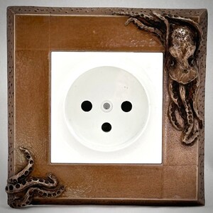May include: A brown outlet cover with an octopus design. The octopus is sculpted in a 3D design and has a textured surface.