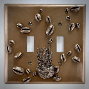 Może przedstawiać: Złoty włącznik światła z rzeźbą filiżanki kawy i ziaren kawy.