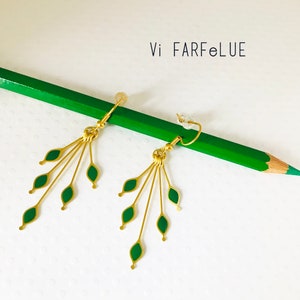 Peut inclure: Boucles d'oreilles en or avec des feuilles en émail vert qui pendent du bas. Les boucles d'oreilles sont sur un crayon vert.