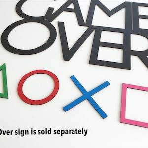 May include: Black "GAME OVER" sign with colourful geometric shapes. The shapes include a green triangle, red circle, blue X, and pink square. The text "Game Over sign is sold separately" is at the bottom.