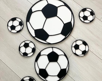 May include: A collection of black and white soccer ball decorations of varying sizes. The soccer balls are arranged on a light wood-grain surface. The design features the classic pentagon and hexagon pattern.