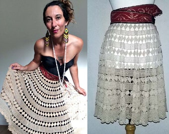 May include: A beige crochet skirt with a scalloped hem and a geometric pattern. The skirt is worn with a black strapless top and a red and gold belt.