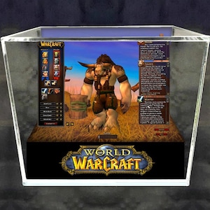 May include: A 3D diorama of a Tauren warrior character from the World of Warcraft video game. The diorama is in a clear acrylic box with a black base. The character is standing in a field of tall grass. The character is wearing brown leather armour and a brown loincloth. The character is holding a large wooden club in their right hand. The character has a large, brown bull's head. The character is looking to the right. The diorama is set against a blue sky background. The World of Warcraft logo is printed on the base of the diorama.