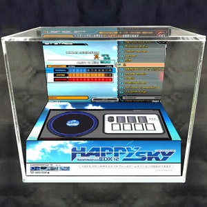 May include: A miniature arcade cabinet with a clear acrylic case, featuring a blue and white Happy Sky beatmania IIDX 12 game screen. The cabinet has a black and silver turntable and a set of buttons.