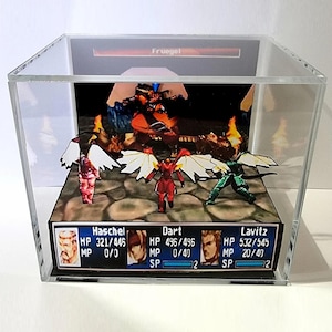 Puede incluir: Un diorama en caja 3D que presenta una escena de batalla de videojuego con tres personajes frente a un jefe llamado Fruegel. La pantalla incluye una interfaz de estado de personaje en la parte inferior que muestra a Haschel, Dart y Lavitz.