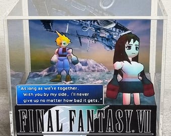 May include: A clear acrylic display cube containing a 3D diorama of Final Fantasy VII characters Cloud and Tifa. The scene features a blue text box with the quote: "As long as we're together. With you by my side, I'll never give up no matter how bad it gets."