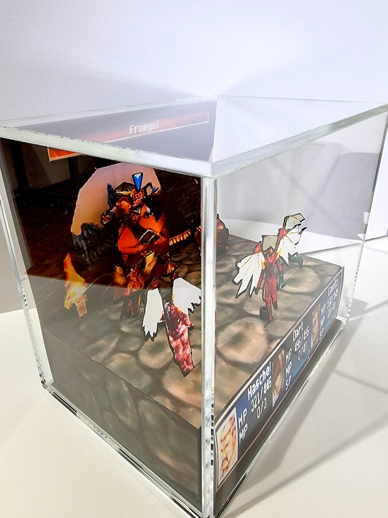 Pode incluir: Um diorama 3D de uma cena de batalha de um videogame com um personagem vermelho e branco com asas e um personagem azul e laranja com uma espada. O diorama &eacute; exibido em um cubo de acr&iacute;lico transparente com uma base preta. O texto "Haschel" e "Dart" &eacute; vis&iacute;vel na base.