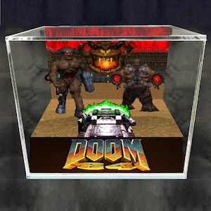 May include: A clear acrylic display cube containing a 3D diorama of the video game Doom 64. The scene features two brown monster figures, a floating fiery head, and a weapon in the foreground. The base displays the Doom 64 logo in yellow and blue.